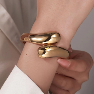 Polished gold irregular fluid open bangle with round drop ends shown on model wrist