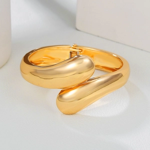 Macro view of polished gold teardrop cuff with hinge closure on geometric background