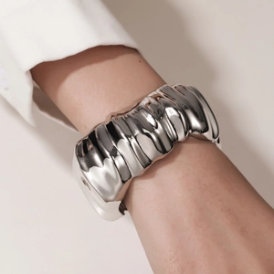 Close-up of a wide irregular wave bangle with polished silver mirror finish on a wrist