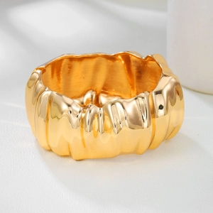 Detailed close-up of wide gold metal cuff with irregular liquid texture and glossy finish