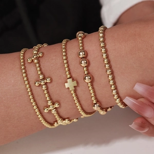 Five-piece gold beaded bracelet set with cross pendant charms worn on a female wrist