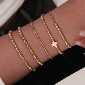 Macro shot of 5-piece gold beaded stretch bracelets with cross charm on wrist