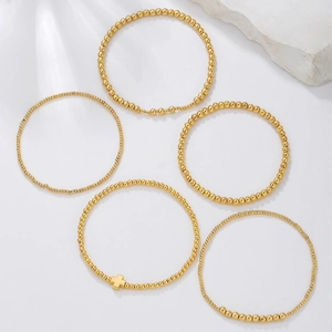 Detail of five-piece gold beaded bracelet set featuring a metallic cross charm on white stone