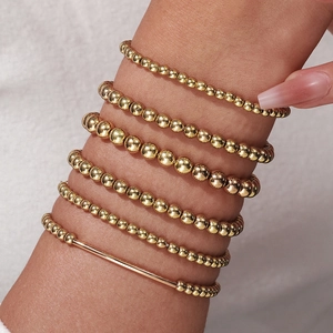Primer plano de pulseras de cuentas doradas apiladas con acabado pulido en tejido