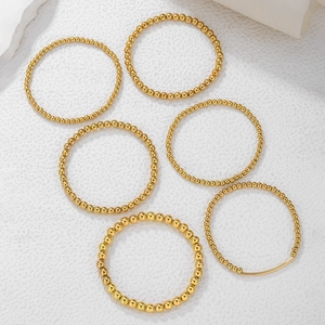 Set de pulseras de cuentas doradas con tubo metálico sobre fondo de mármol blanco