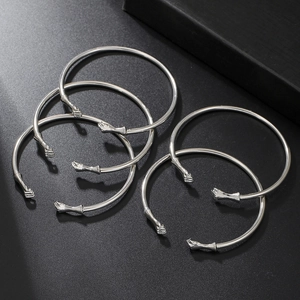 Detail of five silver fist-shaped punk bangles stacked on a matte black surface