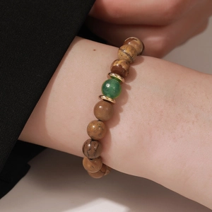 Primer plano de una pulsera de cuentas de piedra marrón con cuenta verde en la muñeca