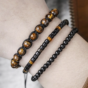 Macro shot of men's triple-layer tiger eye and black onyx beaded bracelets worn on wrist