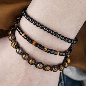 Close-up of men's layered tiger eye and black onyx beaded bracelets on a wrist