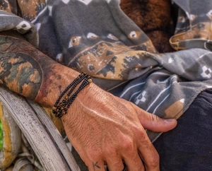 Detailweergave van heren kralenarmband met tijgeroogstenen op een getatoeëerde pols