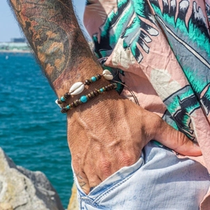 Bohemian men's bracelet set with wooden beads, turquoise, and shells on beach background