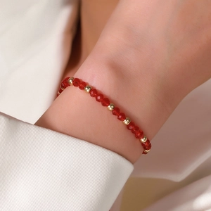Detail van kralenarmband met rode gefacetteerde kristallen en gouden tussenstukjes