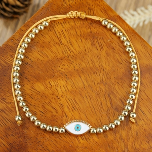 Detail van verstelbare boze oog armband met gouden kralen en emaille bedel op hout