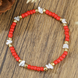 Detail van een kralenarmband met rode, witte stenen en gouden accenten op houten tafel