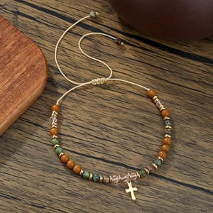 Detail van kralenarmband met stenen kralen en een gouden kruishanger