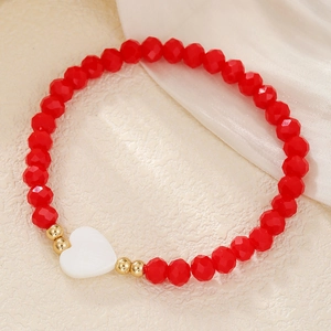 Detail van rode gefacetteerde kralenarmband met hartvormige hanger op witte stof