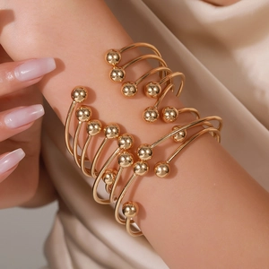 Close-up of stacked gold-plated open bangles with polished beads on a woman's wrist