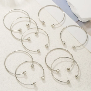 Flat lay of eight minimalist silver plated open bangles with ball ends on textured white background