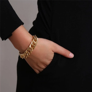 Close-up of a chunky golden Cuban link chain bracelet on a model wrist against black fabric