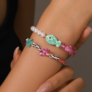 Détail de bracelets perlés d'été avec poissons en céramique et breloques cœur au poignet