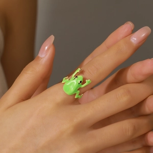 Levendige groene emaille kikkerring met gouden accenten gedragen aan vinger, sieraad