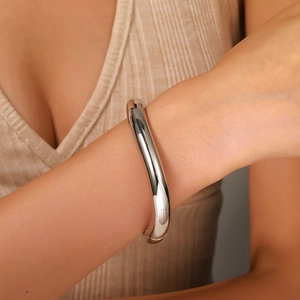 Detail of chunky silver spring hinge cuff bracelet on model wearing beige knitwear