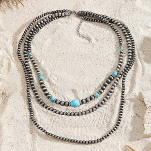 Drielaagse bohemian ketting met turquoise kralen en zilveren details op het zand