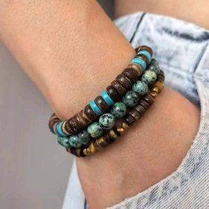Detail of stacked handmade wooden bead bracelets with natural stones on denim background