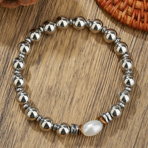 Detail of silver beaded bracelet featuring a white oval pearl inlay on a wooden surface