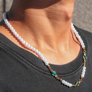 Close-up of pearl necklace with green gemstones worn by a male model on black shirt