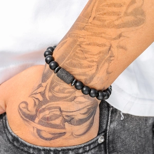 Herenarmband van matzwarte kralen met natuurlijke lavasteen op een getatoeëerde pols