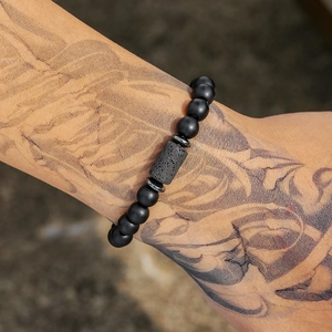 Herenarmband met zwarte matte kralen, cilindrische lavasteen en zilveren accenten op getatoeëerde arm