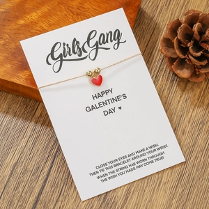 Detail eines goldenen Herz-Charm-Armbands mit roter Emaille auf einer Geschenkkarte