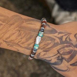 Macro shot of bohemian beaded bracelet with turquoise stones and silver charms on tattooed arm