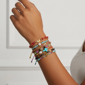 Primer plano de pulseras boho apiladas con dijes de corazón dorado y cruz azul
