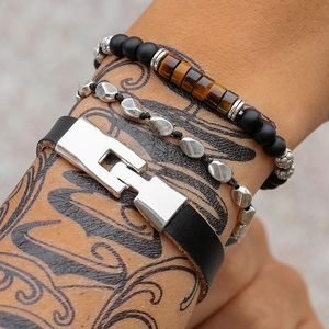 Dettaglio del bracciale con pietre occhio di tigre e polsino in pelle su braccio tatuato