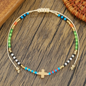 Detalle de pulsera de cuentas de colores con cruz dorada y cierre de cordón ajustable
