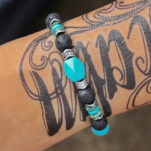 Macro-opname van een turquoise kralenarmband met lavastenen op getatoeëerde pols