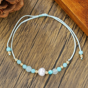 Detalle de pulsera de amistad tejida azul con perla de agua dulce y piedras naturales
