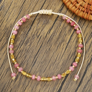 Detalle de cuentas de cristal rosa y acentos dorados en pulsera de la amistad tejida a mano