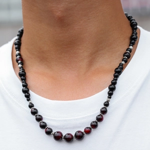 Dettaglio della collana con occhio di tigre rosso e perle nere indossata su t-shirt