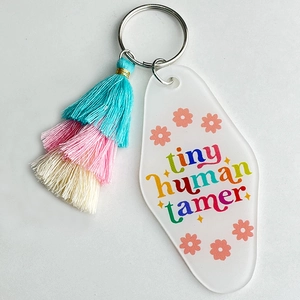 Detail of white motel keychain with Tiny Human Tamer text and a triple-layered tassel