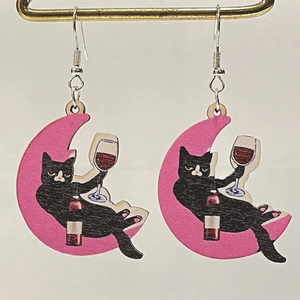 Detail of wooden earrings showing a black cat holding a wine glass on a pink crescent moon