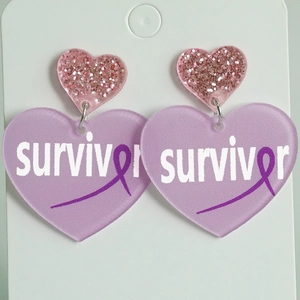 Detail of pink glitter and purple acrylic heart earrings with survivor text and ribbon