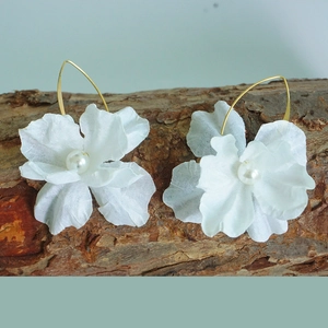 Detail der Blumenohrringe mit weißen Blütenblättern und Perle auf rustikaler Rinde