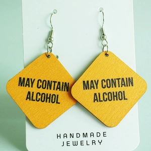Vue détaillée de boucles d'oreilles en bois jaune avec le texte MAY CONTAIN ALCOHOL