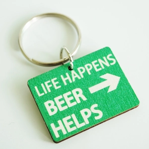 Green wooden keychain with Beer Helps slogan and metal ring on gray background