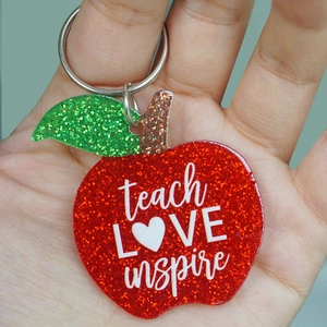 Handheld view of red glittery apple keychain with teach LOVE inspire text for teachers
