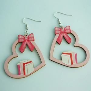 Dettaglio di orecchini a cuore in legno con fiocchi rosa a pois e motivi di libri