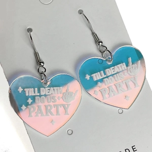 Makroaufnahme herzförmiger schillernder Acryl-Ohrringe mit Till Death Do Us Party Text